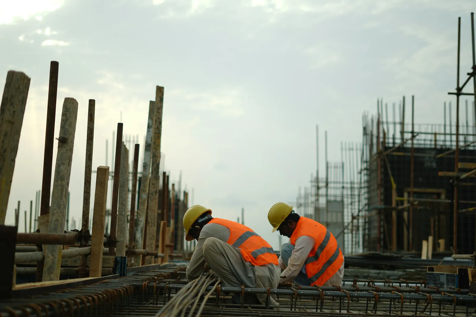Two workers in hard hats tying reinforcement bars on a site